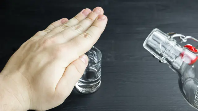 A hand reaching to stop a glass of alcohol